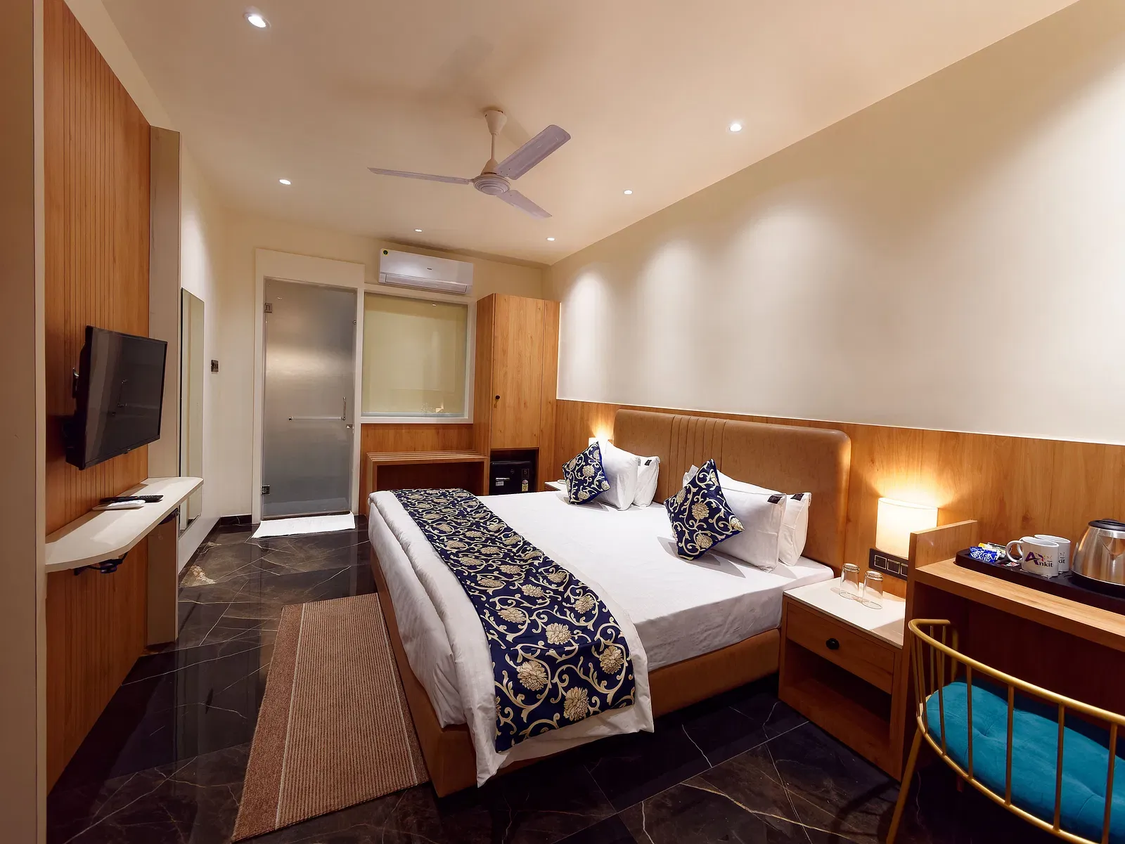 Image of deluxe room with a bed with table and chair on the side of the table and a fan on te ceiling at Ankit Hotel, Jabalpur