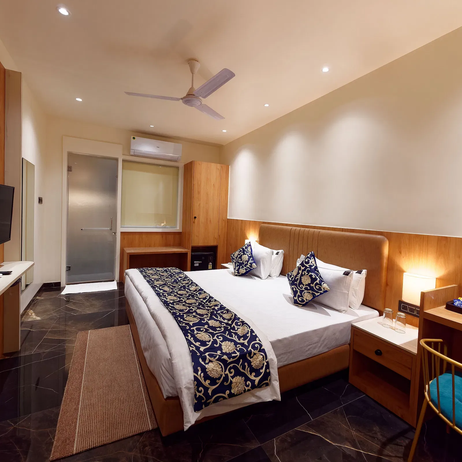 Image of deluxe room with a bed with table and chair on the side of the table and a fan on te ceiling at Ankit Hotel, Jabalpur