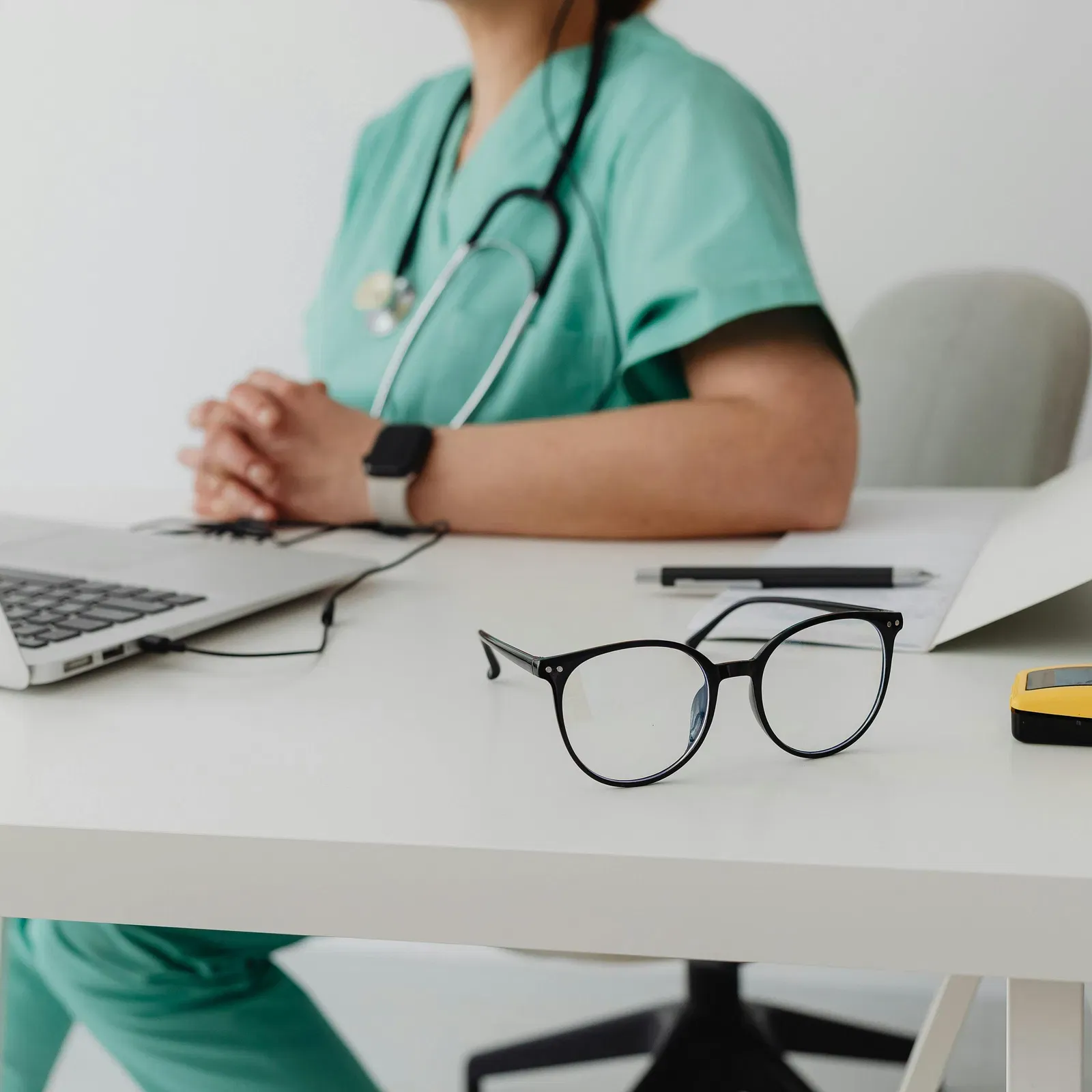 A doctor in scrubs sitting at their desk working on a laptop