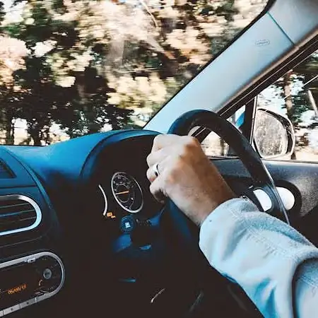 Image of a person driving a car with trees in the background